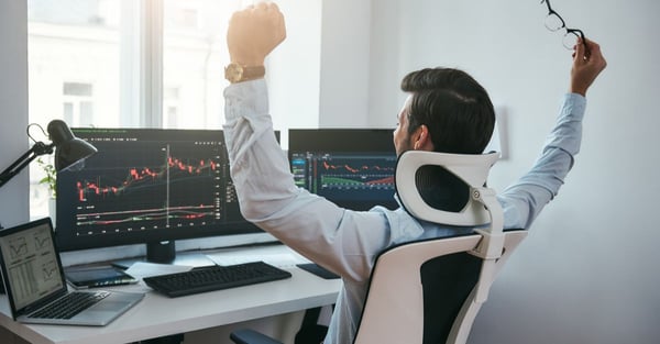 back view of a man with both hand raised in celebration while watching trading charts