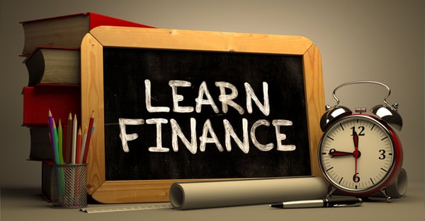 The phrase Learn Finance Handwritten on a Chalkboard, next to a stack of Books, Alarm Clock and Rolls of Paper